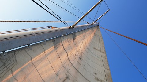 A mainsail is filled with a light breeze. Bright blue sky as a background. Onboard a sailing yacht.