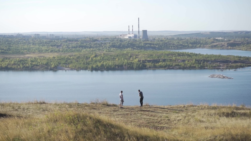 Young hipsters stand at the edge of the valley and gaze into the distance. One of them points his hand to the side and leaves