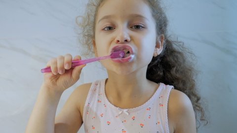 Portrait happy cute young teenage girl brushing teeth in bathroom and smiling. Children daily healthcare routine. Caucasian kid with white tooth looking at mirror isolated at home. Lifestyle.