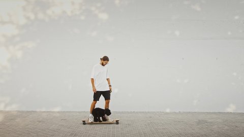 Hipster guy riding his dog on skateboard, outdoor shot