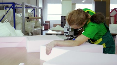 An female worker cutting foam rubber for the production of a sofa in a furniture factory. 4K