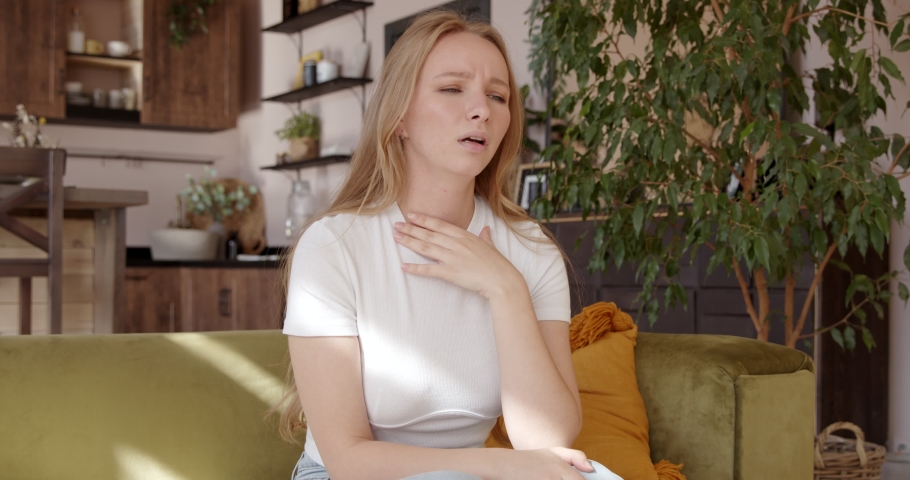 A young woman holds her hands over a sore throat. Painful neck and frowning, thyroid disorders, suffering sore throat, tonsils inflammation. Royalty-Free Stock Footage #1058926718