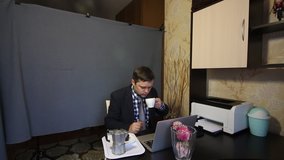 Eating during a video call. A man in a business suit is talking via video communication. Communicating, he drinks coffee. Nearby on a tray is a coffee maker and a muffin