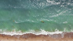 Unrecognizable people having fun jumping on waves at Black Sea Ukraine beautiful beach top down aerial angle. Muddy water brown sand