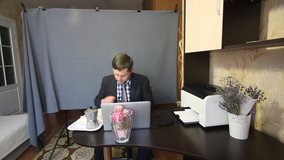 Eating during a video call. A man in a business suit is talking via video communication. While communicating, he gestures and drinks coffee. Nearby on a tray is a coffee machine with coffee