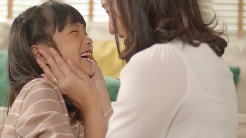 Happy little Asian Cute Girl hugging, kissing, and embracing her mom enjoying, bonding, and laughing together. Mother parent hugging her kid having a tender and lovely moment in living room at home