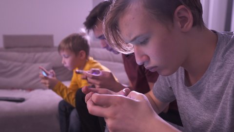 Children with smartphones at home. Three boys spending time in a social network using mobile phones. White kids using cell phones for gaming. Lifestyle concept. Full hd real time footage.  