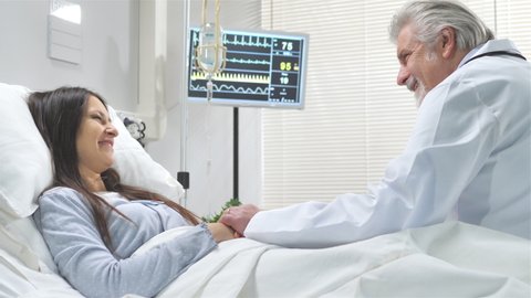 caring doctor visits mature woman on hospital bed,friendly doctor holding patient hand and talking to her,positive feeling good news