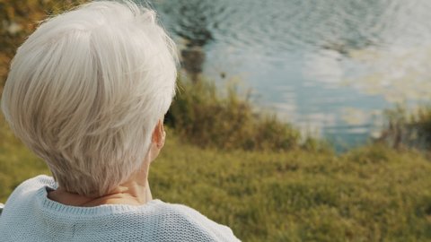 Close up, senior gray haired woman in the wheelchair enjoying autumn breeze near the river. High quality 4k footage