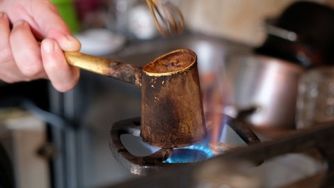 Making turkish coffee in copper cezve over gas stove. Milling of grains. On the gas stove Turk with a running coffee. Running coffee close up. gas stove with burning fire. A cup of coffee