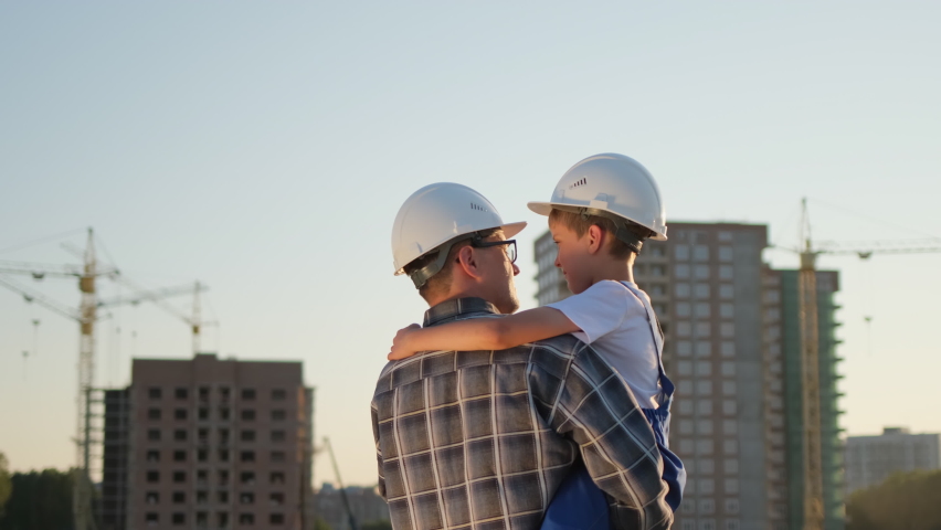 Father and son happy Family concept. Little boy and his dad engineer builder architect with safety helmets, on background new buildings and construction cranes on site. Future profession, 4 K slow-mo Royalty-Free Stock Footage #1058944418