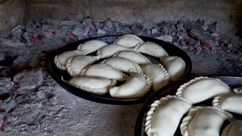 Uncooked traditional Argentinian empanadas inside a clay oven surrounded by burning ashes