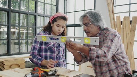 Grandfather and granddaughter are training carpenter. Happy family activities within home. Senior carpenter is teaching and apprentice  young girl with great skill. Concept Education and career