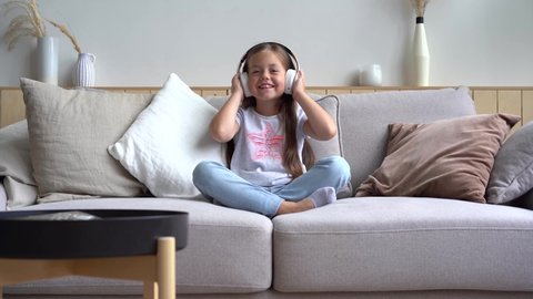 Cute little girl listening to music in headphones while sitting on the couch