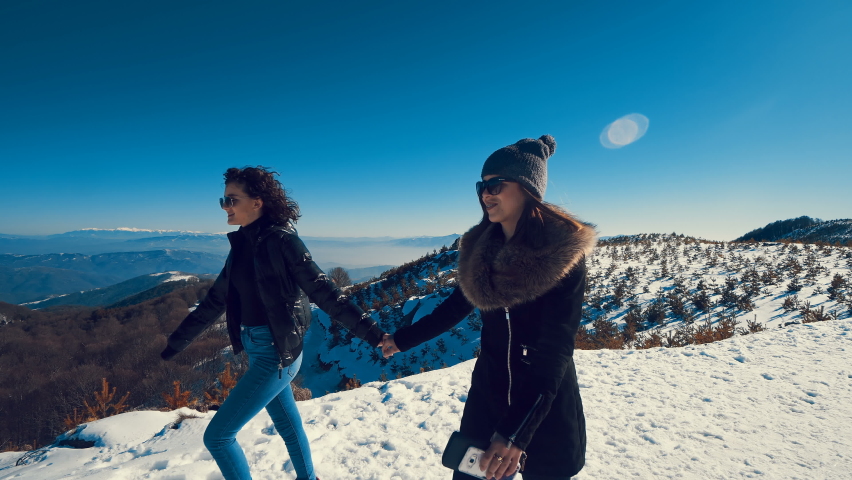 Attractive beautiful girl teens walking over snowy holding their hands and laughing, mountain landscape at background