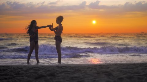Two girls exercise, training karate on ocean beach against sunset sky and rolling waves