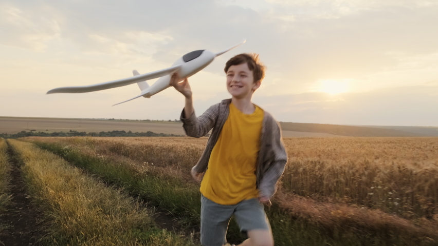 Happy boy runs of Wheat Field  holding airplane in his hand run on summer meadow of sunset of summer day towards bright sun slow motion. Child plays lifestyle. Childhood. Agro Farm. Go Everywhere Royalty-Free Stock Footage #1058966798