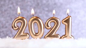 The text of the number 2021 in the snow, on a silver blurred iridescent background with bokeh. Burning candles 2021. Christmas or New Year concept. Selective focus. Video clip hd.