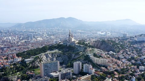 Panoramic aerial view of Notre-Dame de la Garde church and Marseille cityscape. Grand basilica the bell tower landmark at the city's highest point, crowned by golden statue of Mary in France 4K