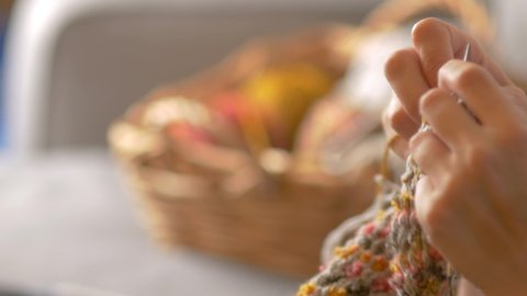 Close up of hands knitting, with basket of yarn in background.  Lifestyle shot with slow pan of at home crafting, making a garment from wool.