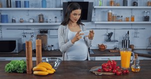 Pregnant woman taking photo with smartphone near vegetables in kitchen