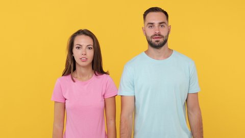 Young couple friends bearded man woman 20s in basic t-shirts posing isolated on yellow background studio. People lifestyle concept. Dancing fooling around having fun expressive gesticulating hands