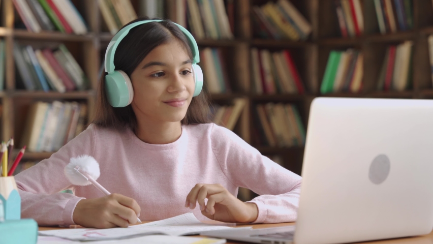 Happy indian latin preteen girl school pupil wearing headphones raising hand distance learning online at virtual lesson class with teacher tutor on laptop by video conference call studying at home. Royalty-Free Stock Footage #1058989073