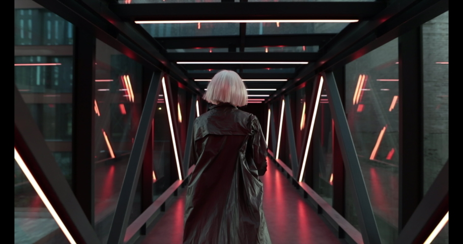A woman runs and looks around in a futuristic neon tunnel. Cyberpunk. High quality 4k footage Royalty-Free Stock Footage #1058992109
