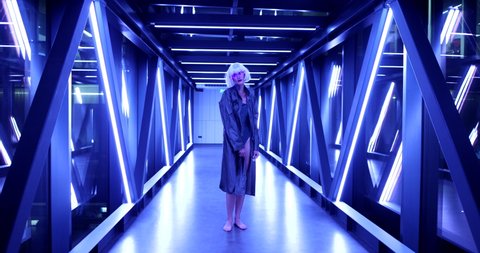 Blonde in blue neon and futuristic clothes. Cyberpunk and the fashion of the future. High quality 4k footage