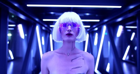 A woman in cyber glasses walks through a neon tunnel. High quality 4k footage