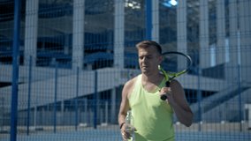 Man Drinking Water and pouring on face After Hard Exercising And Playing Tennis. Portrait Of Young Tired Sportsman In Sportswear Enjoying Drink On Outdoor Court. Healthy Lifestyle. Man wash his face
