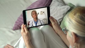 Woman sits on couch at home talking to remote doctor telemedicine with tablet computer. Doctor listens intently.