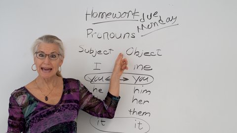 Extreme closeup portrait of smiling mature woman english grammar teacher, set against a whiteboard in a school classroom.