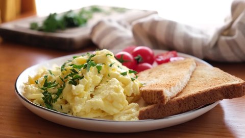 Garnish scrambled eggs with chopped parsley. Female chef hand add parsley to breakfast eggs omelette