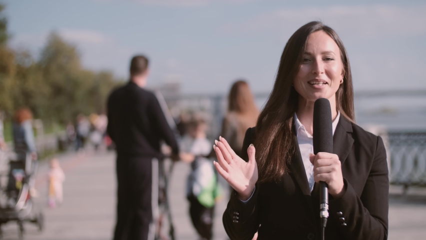 TV reporter speaks with a microphone in the street talking about how people with their families came to the city's embankment in the park after quarantine. | Shutterstock HD Video #1058996060