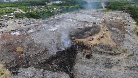 Aerial view of firemen, fighting a fire at a junkyard, smoke rising in middle of piles of trash, in Evento, Santo Domingo, Dominican Republic - Static drone shot