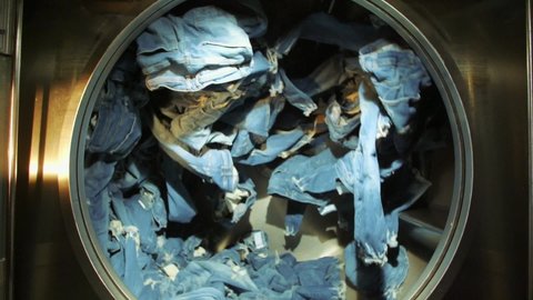 Slow motion shot of blue jeans spinning inside an industrial washer dryer in jeans factory.