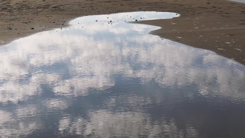 Sky reflection on surface of water in puddle on sandy summer sea beach. Abstract natural 4k video background.