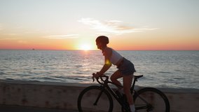 Young stylish brunette woman rides bike on coastline at sunrise. Brunette girl in helmet glasses and stylish clothes is pedaling on bicycle at sunset - Powered by Shutterstock - Get 15% off with code: PIKWIZARD15