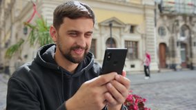 Portrait of business man reading message with smart phone in outdoor. Using smartphone for video calls. Looking at screen, smiling, gesturing. Connection concept. Close up businessman having chat