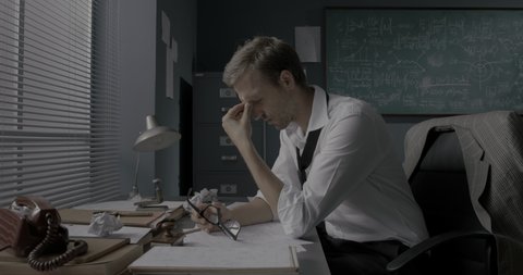 Stressed mathematician sitting at office desk and checking his papers, he can't find a solution to a math problem