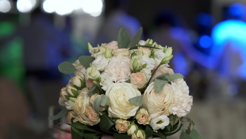 Wedding bouquet on the table in the Banquet hall. Guests dance in the background in blurred out of focus. | Shutterstock HD Video #1059012806