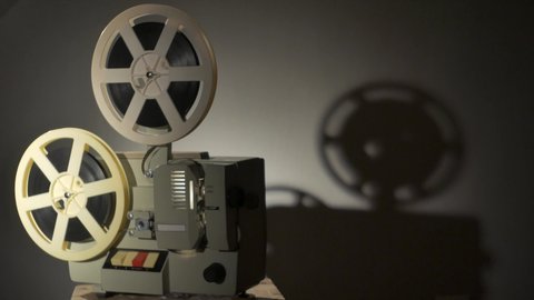 Old film projector shows a film, in a dark room.
