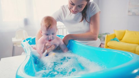 mother touching infant son playing with toy while taking bath in baby bathtub