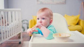 infant kid sucking spoon with baby food near bowl on table
