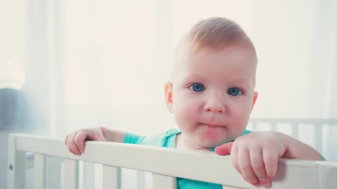 joyful infant boy standing in baby crib and looking at camera