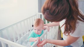 brunette mother touching and looking at infant son in baby crib