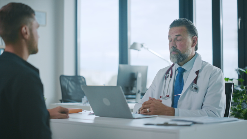 Family Doctor is Delivering Great News About Male Patient's Medical Results During Consultation in a Health Clinic. Physician in White Lab Coat Sitting Behind a Computer in Hospital Office. | Shutterstock HD Video #1059016310