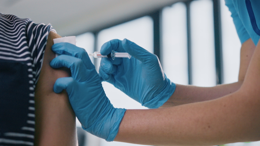 Medical Nurse in Safety Gloves and Protective Mask is Making a Vaccine Injection to a Male Patient in a Health Clinic. Doctor Uses Hypodermic Needle and a Syringe to Put a Shot of Drug as Treatment. Royalty-Free Stock Footage #1059016346