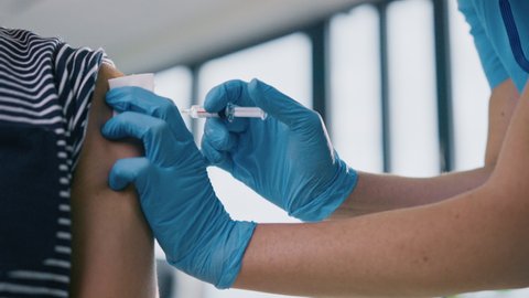 Medical Nurse in Safety Gloves and Protective Mask is Making a Vaccine Injection to a Male Patient in a Health Clinic. Doctor Uses Hypodermic Needle and a Syringe to Put a Shot of Drug as Treatment.